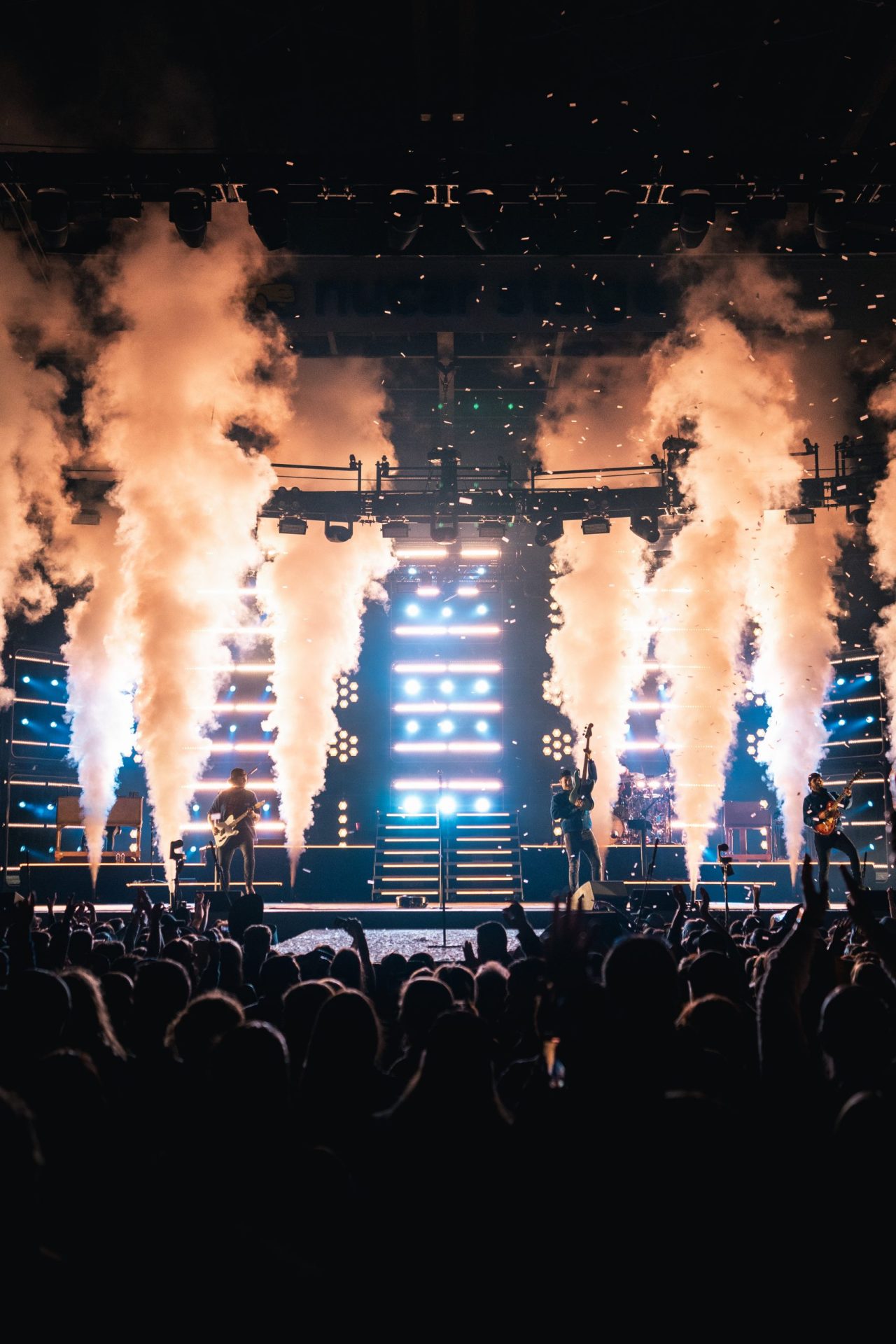 A band rocks out on stage with bold lights and smoke. Fans cheer from the dark, making for a high-energy concert on a budget.