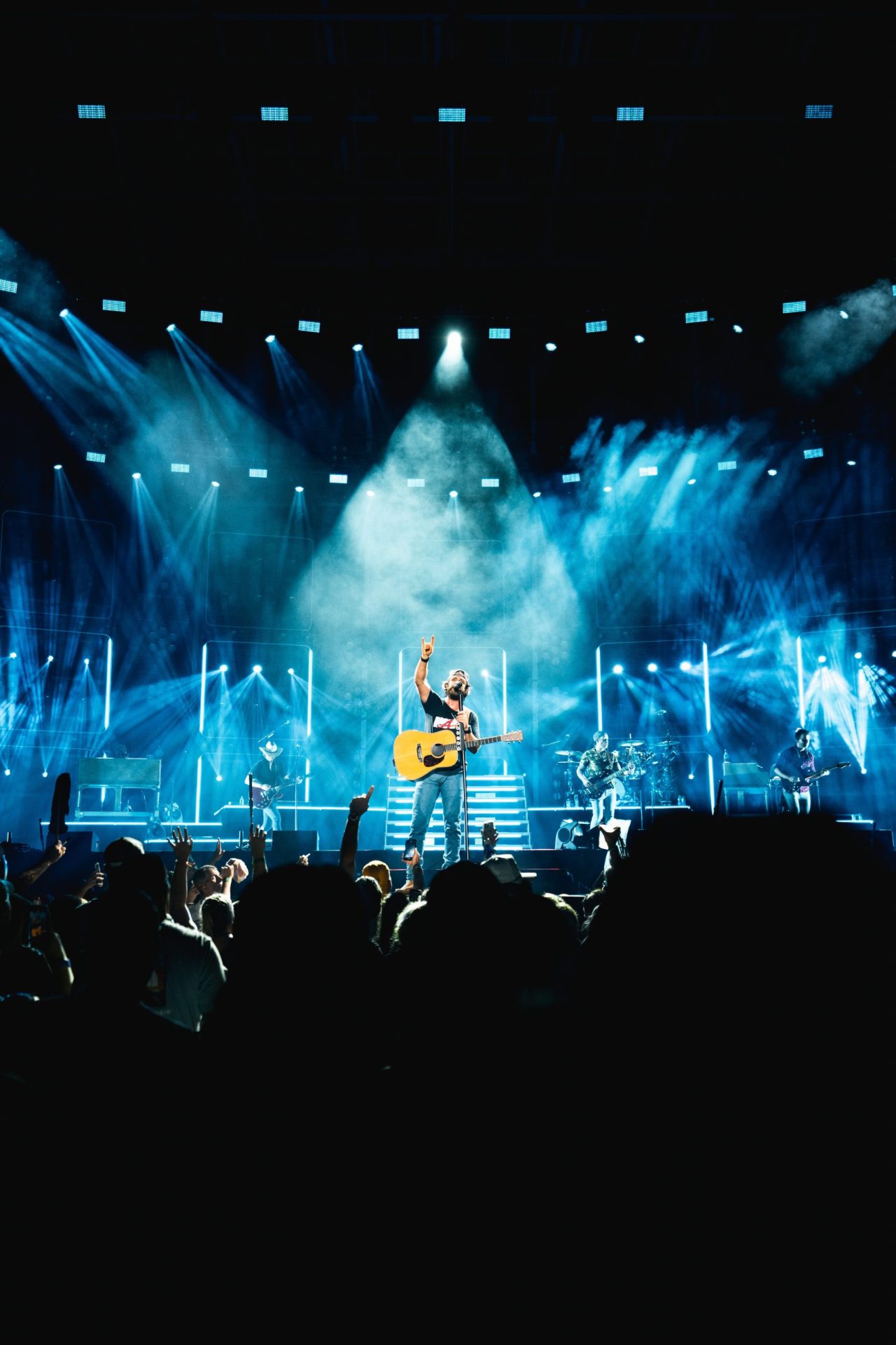 Musician rocking out center stage under bold lights, guitar in hand; lively crowd and bandmates complete the budget concert buzz.
