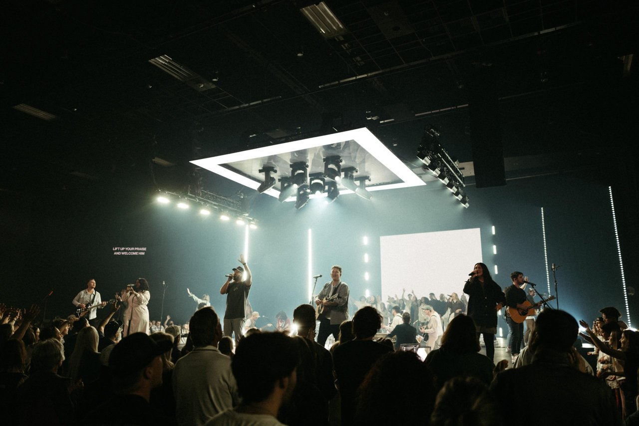 A budget-friendly concert with a band rocking guitars, bright stage lights, a pumped-up crowd, and big screens overhead.