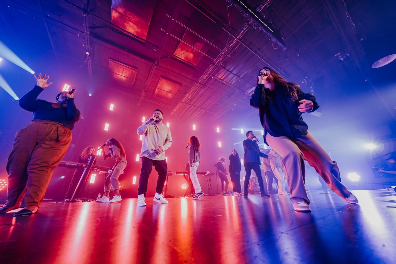 Musicians and singers rock out on stage, moving and singing under bold lights and fog—classic live music energy on a budget trip.