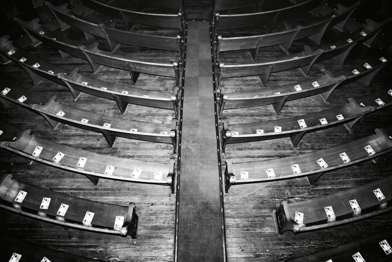 Rows of empty curved wooden theater seats with white tickets—classic budget travel vibes in black and white, ready for adventure.